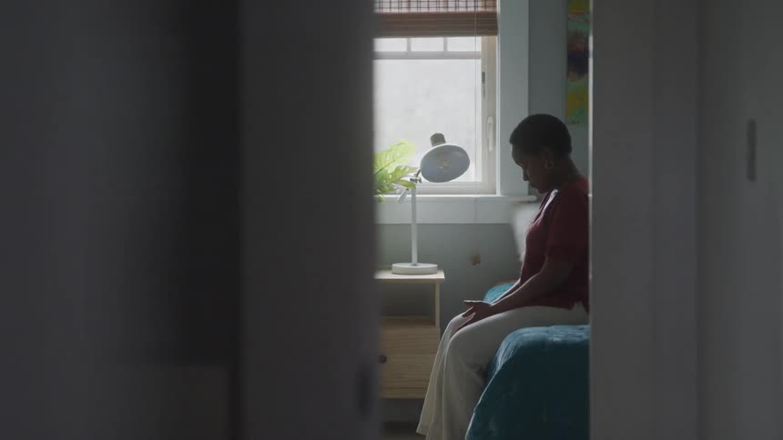 A woman sits thoughtfully on a bed in a cozy modern bedroom at home