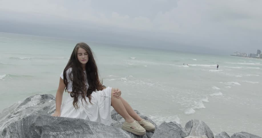 Woman sitting on rocks overlooking an ocean beach