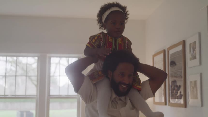 A father is lifting his daughter on his shoulders in the living room