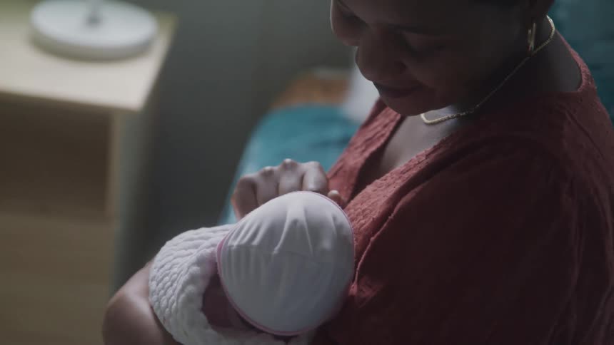A mother is holding her baby in her arms while smiling and touching the babys face