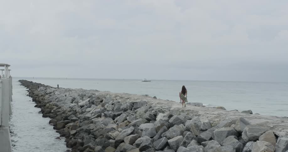 Woman walking on a rock path out into the ocean