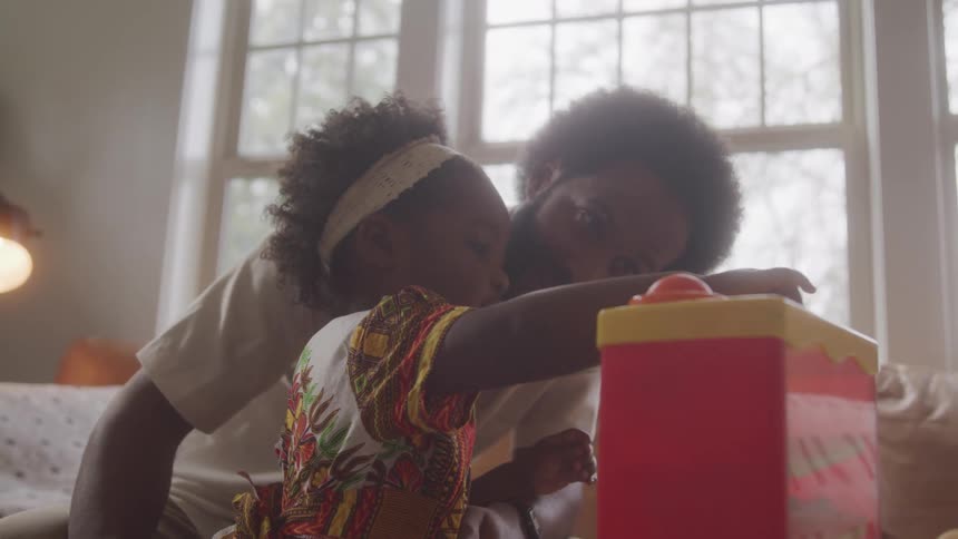 Little girl playing with a toy as father watches in living room