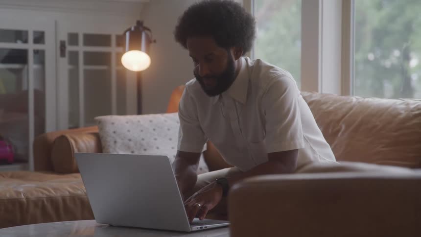 Man sitting in living room staring at laptop open in front of him