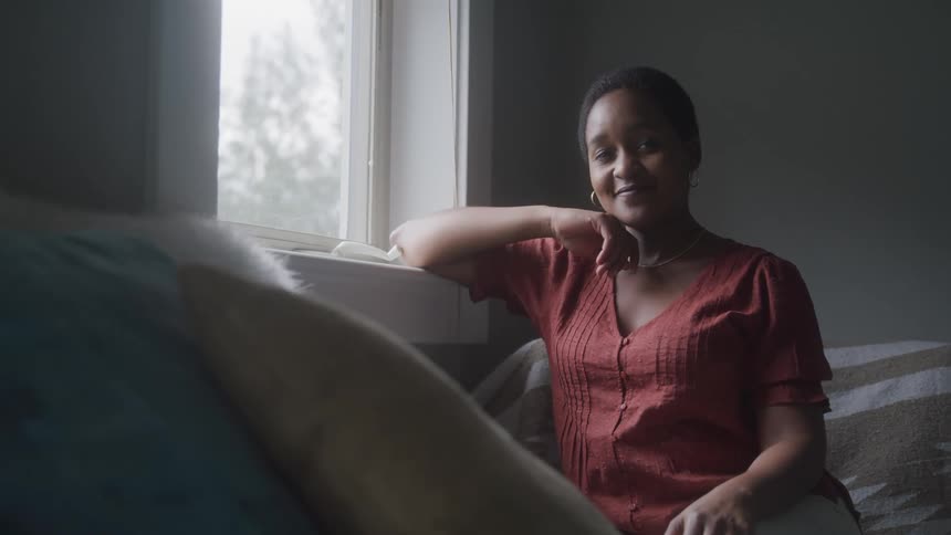 A woman wearing a red shirt sits on a couch near a window