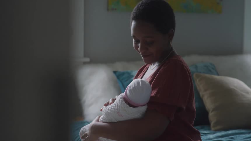 Mother with happy facial expression sitting on the bed in a bedroom holding a baby on her lap