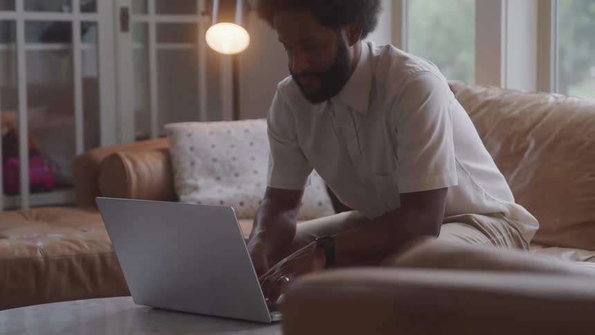 Man sitting on living room couch typing on laptop