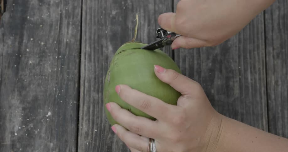 Woman cutting the top off of coconut with knife