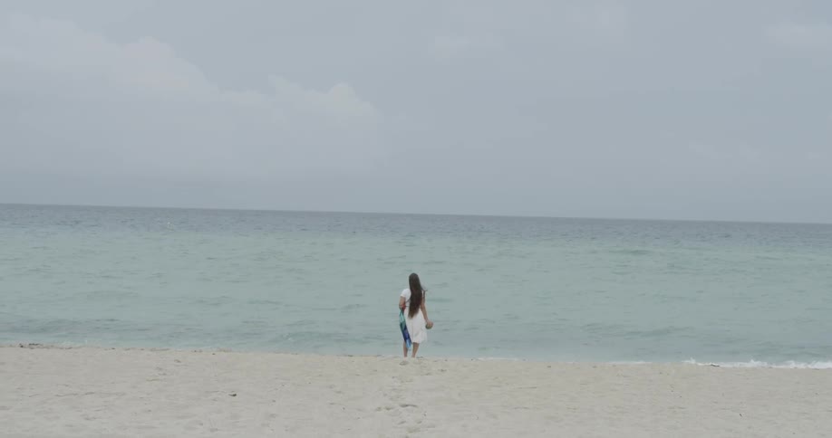 Long-haired woman standing at the water's edge on a beach on a cloudy day