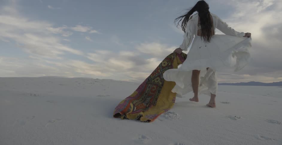 Woman in white dress is walking and dragging shawl in the sand