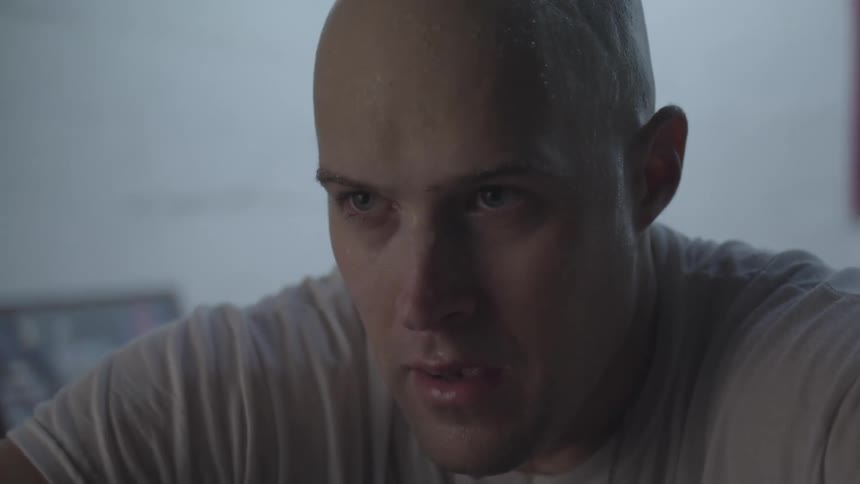 A close up of the face of a bald young man wearing a shirt with visible breath coming out of his mouth