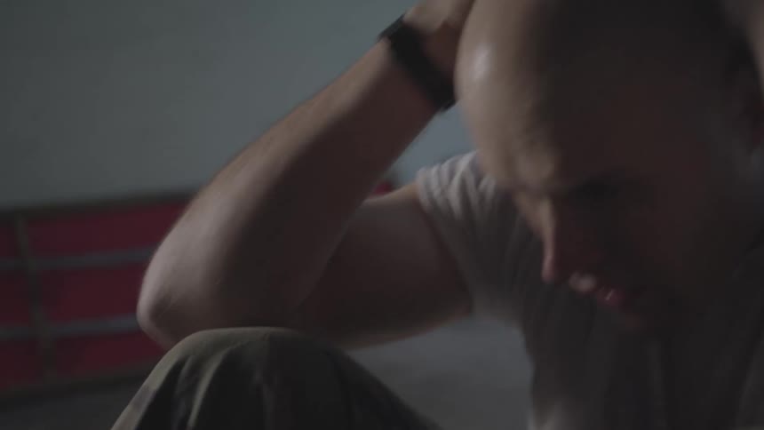Bald man in tee shirt does sit ups on the floor of a room