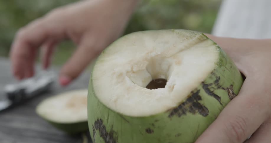 A woman holds a cut green coconut