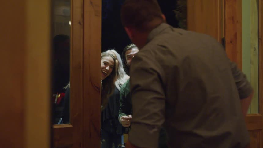 Man opening his front door at night and welcoming a group of excited friends
