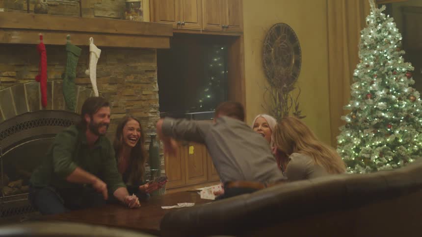 Two men clapping their hands as they sit in a living room playing cards with three other women