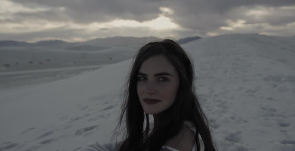 A woman standing in the desert with white sand and staring at the camera