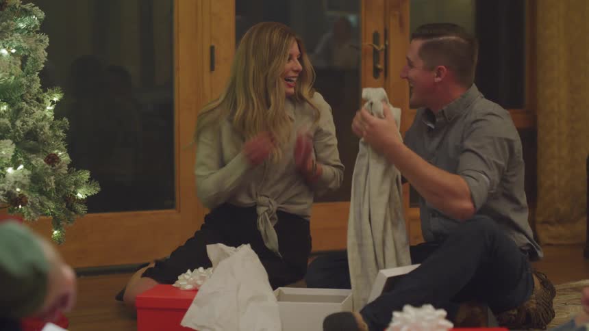 Man sitting next to a woman thanking her for the christmas gift he received and giving her a hug