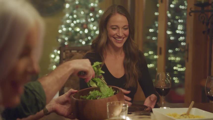 Group of people sitting at a dining table happily serving food to each other