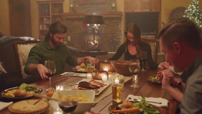 Friends holding hands around the table saying grace before eating