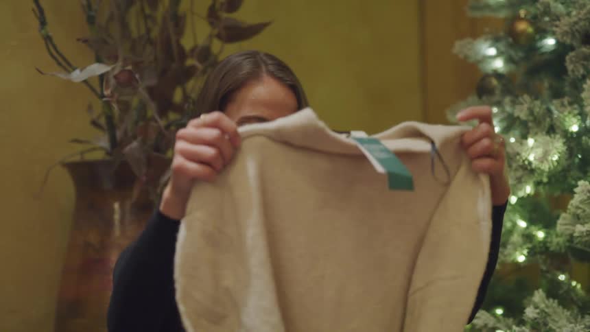 Excited wife opening christmas gift from husband and pulling out a sweater