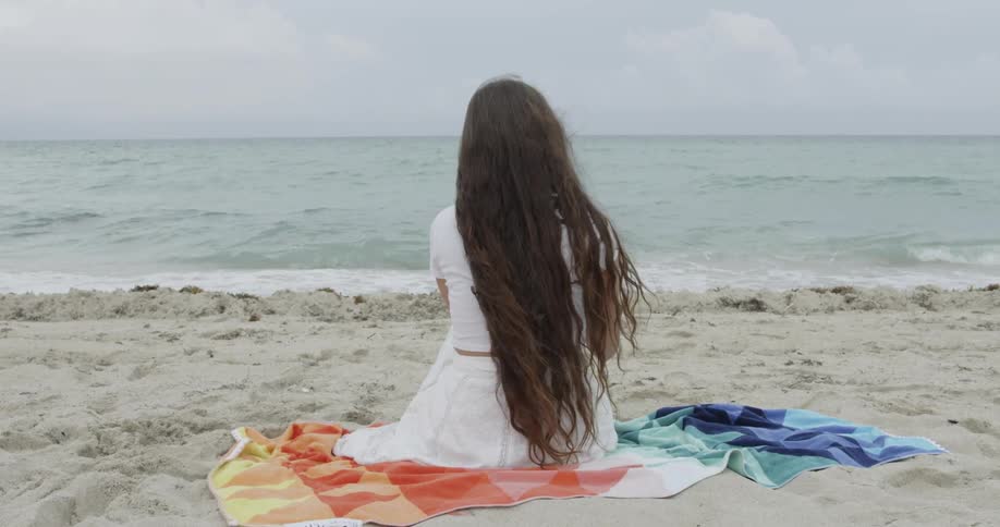 Woman sitting on towel on beach drinking from coconut