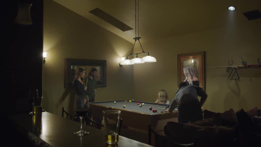 A group of adult friends are playing pool in an indoor recreation room
