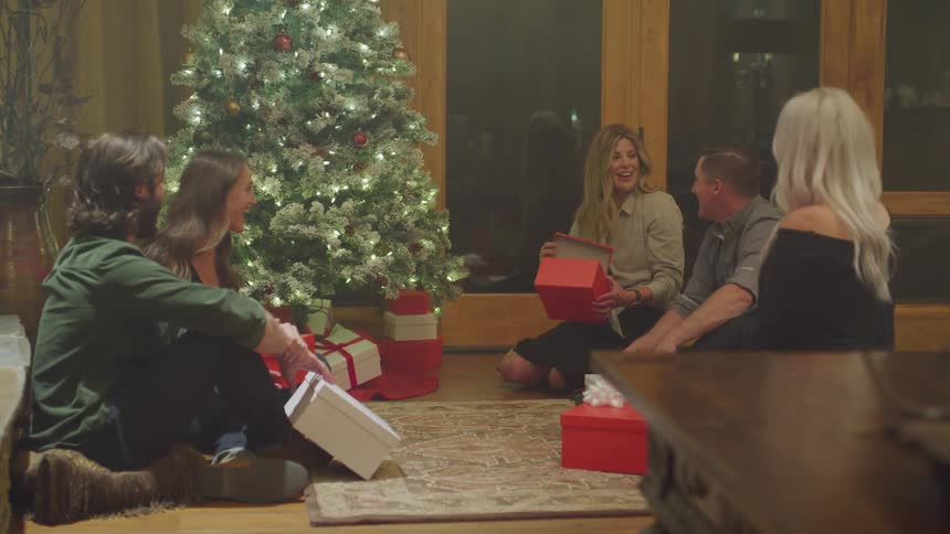 Men and women sitting in living room exchanging christmas gifts