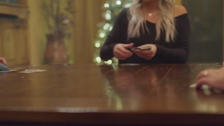 Woman sitting at table dealing cards from a deck to other people