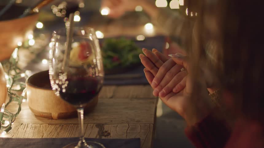 People holding hands at a dinner table at night
