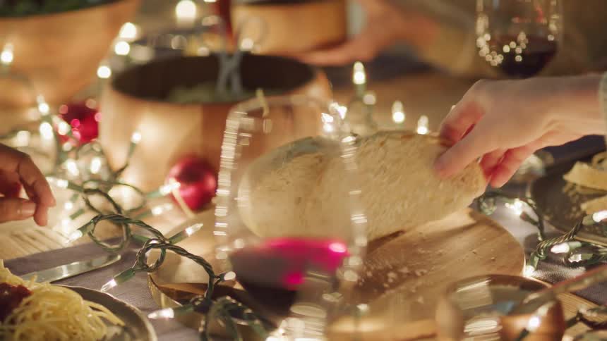 Hands picking up slices of bread on a table with glasses of red wine