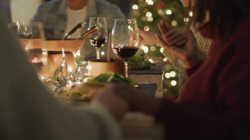 People holding hands and praying before starting to eat at a dinner table