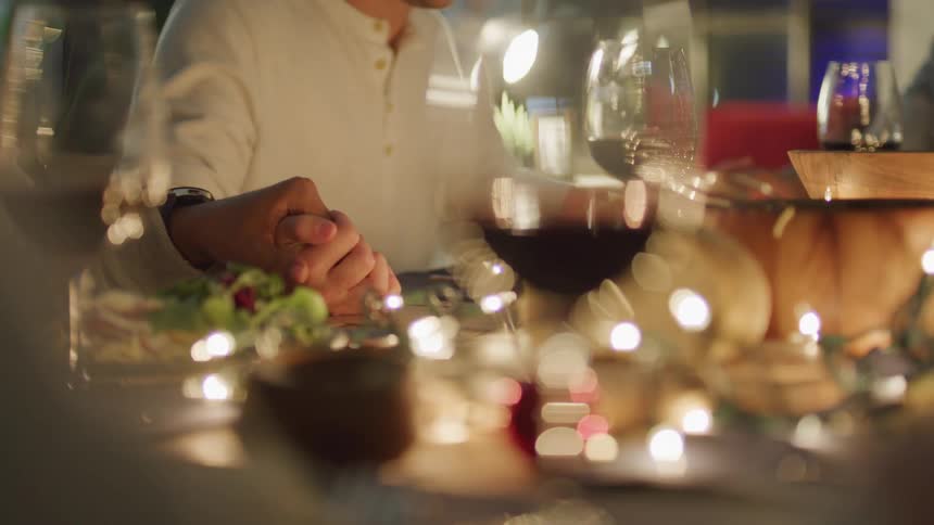 Table with glasses of wine and people holding hands to pray