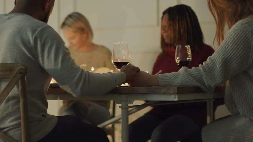 Group of people holding hands while praying at a dinner table