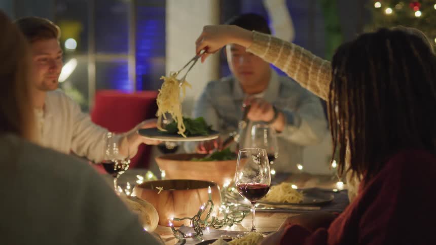 People at a dinner table serving themselves with pasta and glasses of wine on the table