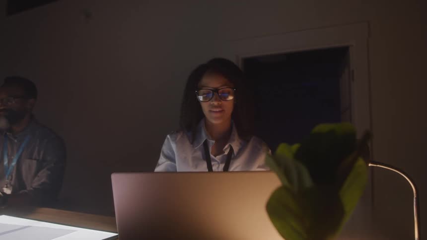 Woman sitting at an office desk in a dark room typing on a laptop