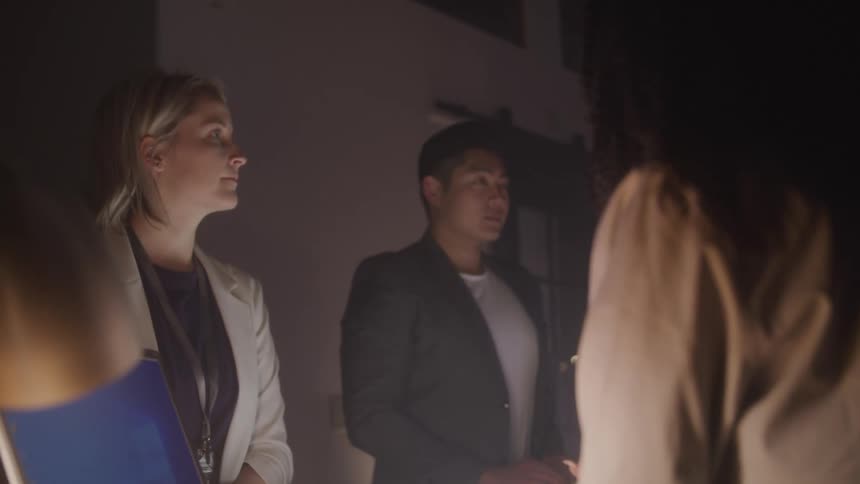 Three individuals stand in a dimly lit room illuminated by a soft light emanating from the desk