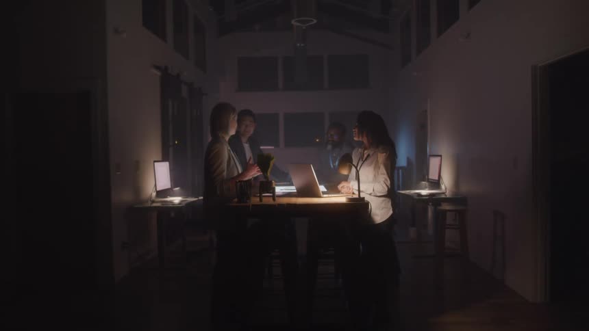Small group of workers at a table with open laptops in a dark room