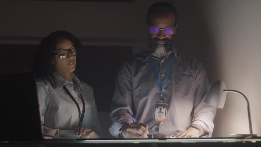 Man and woman working on illuminated screen on table in dark room