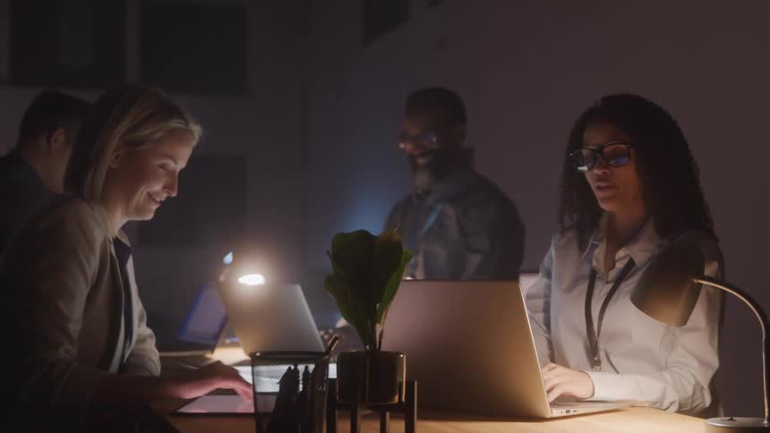 Group of four people including men and women working at a table with tablet and laptops open