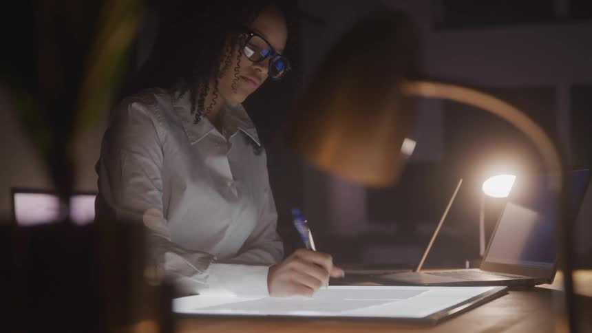 Woman in a lowlit room writing with a digital pen on a tablet on a table