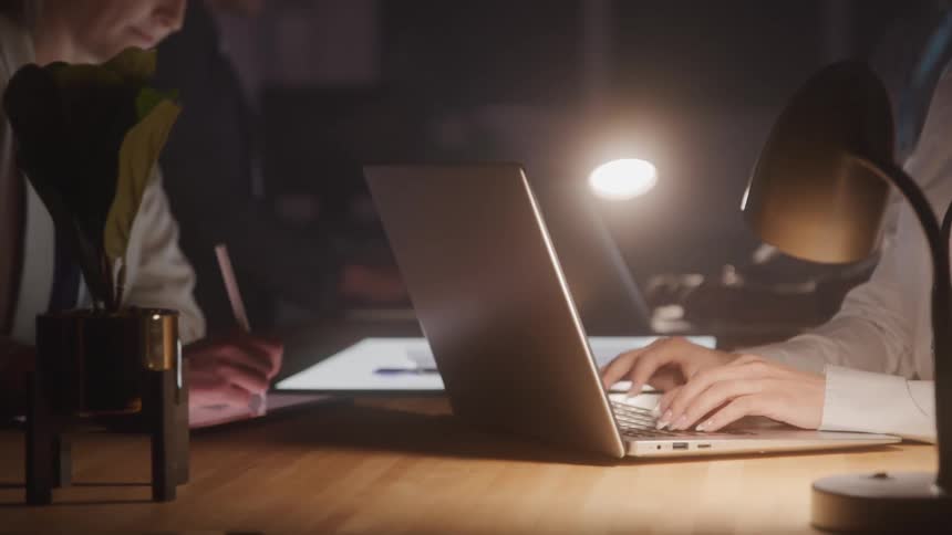 Group of people sitting at a table in low lighting typing on laptop