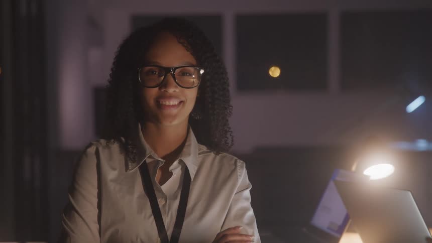A woman stands on a dimly lit office at night looking at the camera
