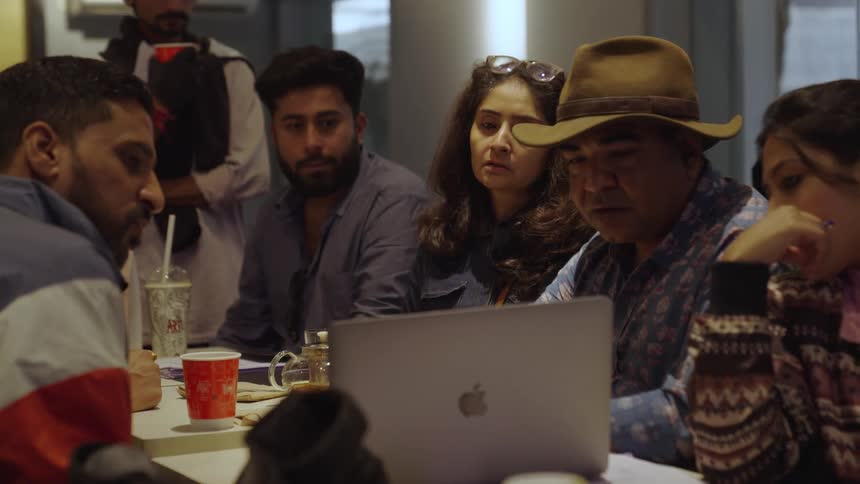 A group of people are intently focused on a laptop screen in a dimly lit room