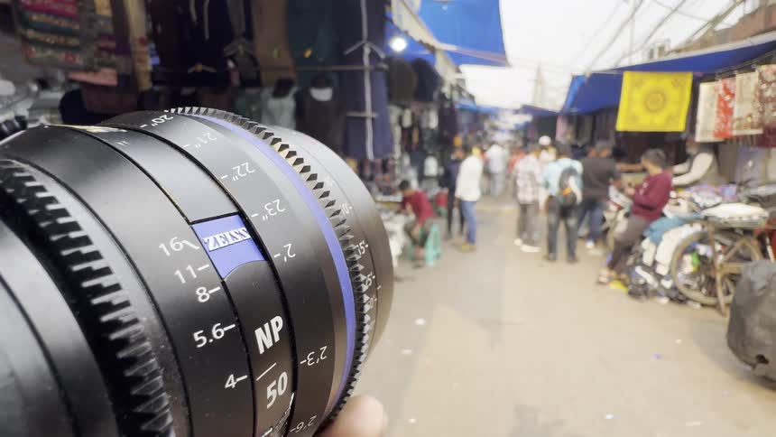A photographer is adjusting a large manual lens likely on location amidst a bustling crowd