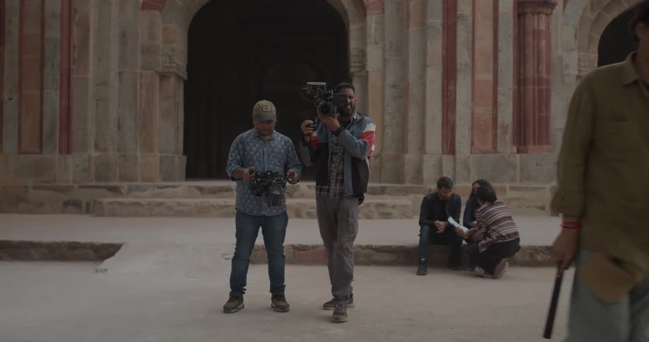 A film crew is shooting a scene outdoors amidst ancient architecture