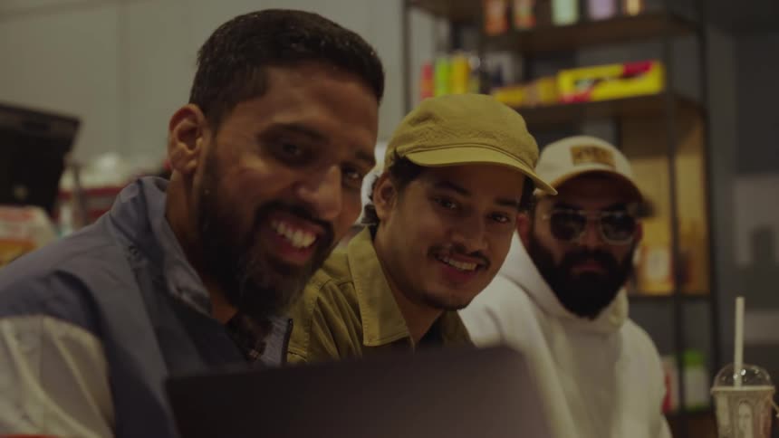 A group of people sits around a table with a laptop drinks and papers actively engaging in a discussion