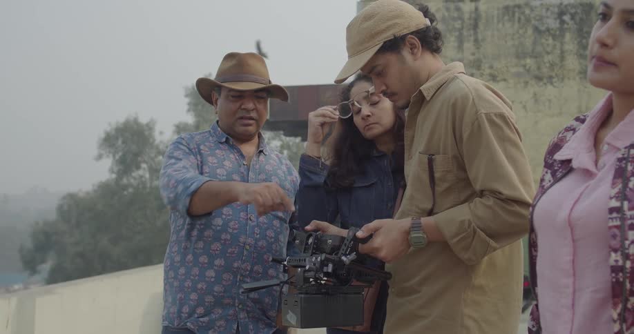 A group of people are examining a camera on a cloudy outdoor set