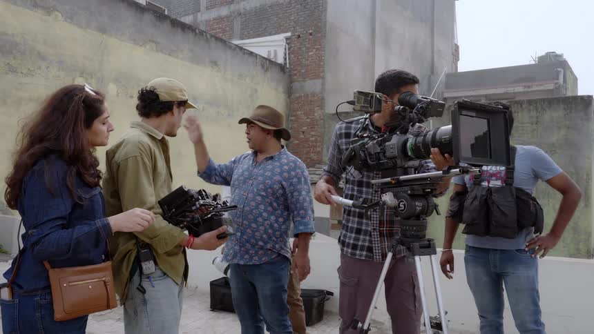 A group of people are on a film set with a camera and lighting equipment