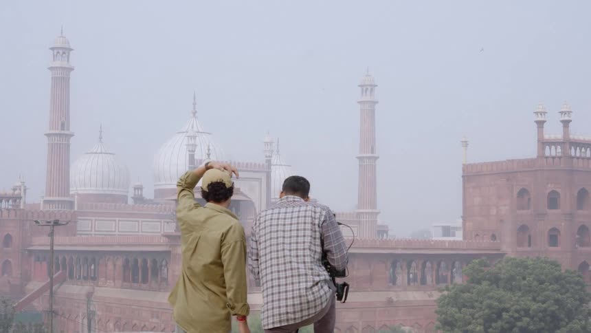 A film crew is shooting a scene against the backdrop of a historic building likely a mosque on a cloudy day