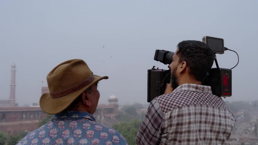 A film crew films a historic building adorned with domes and minarets in the background