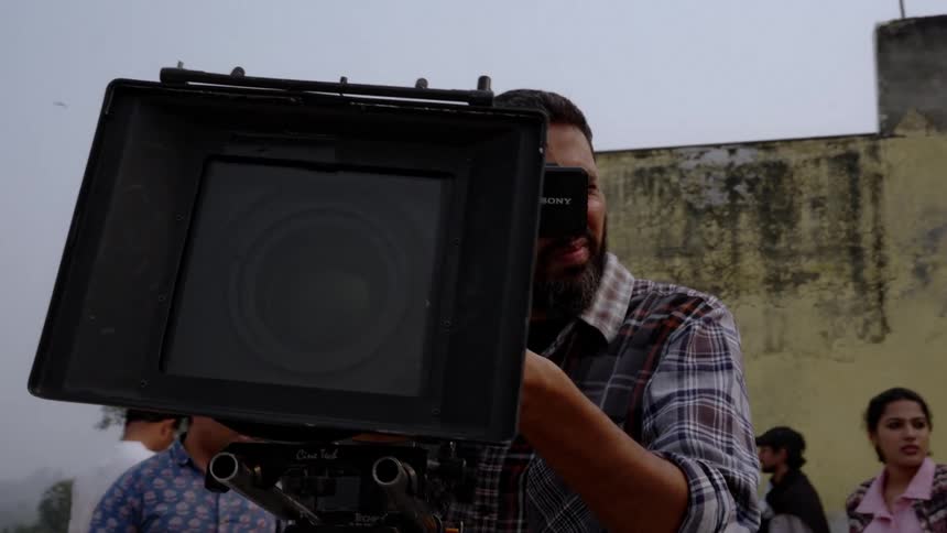 Filmmaker adjusting a professional video camera in an outdoor setting with people around